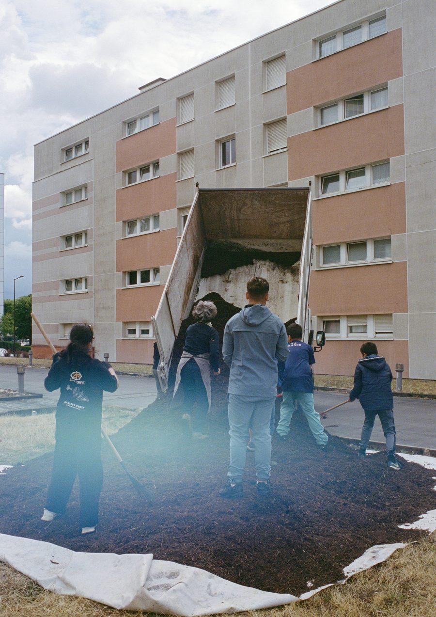 les participant·es remplissent un bac de terre devant l’immeuble