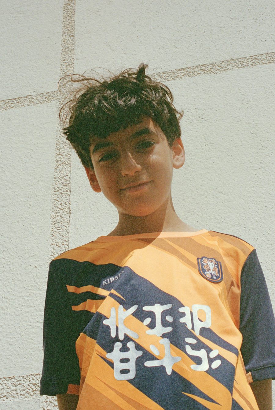 un garçon en maillot orange devant un mur clair